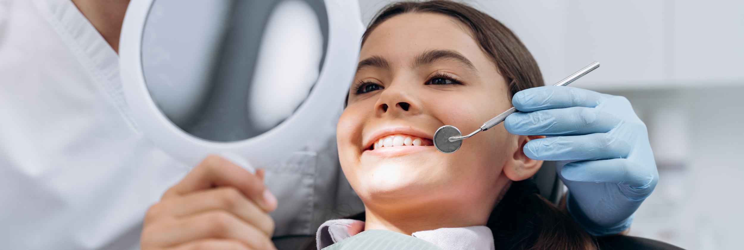 A young girl smiles at herself in a hand held mirror at odonto dental